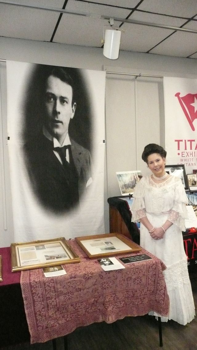 Photo of Mrs Thomas Andrews standing in front of a large image of Thomas Andrews and near a display table